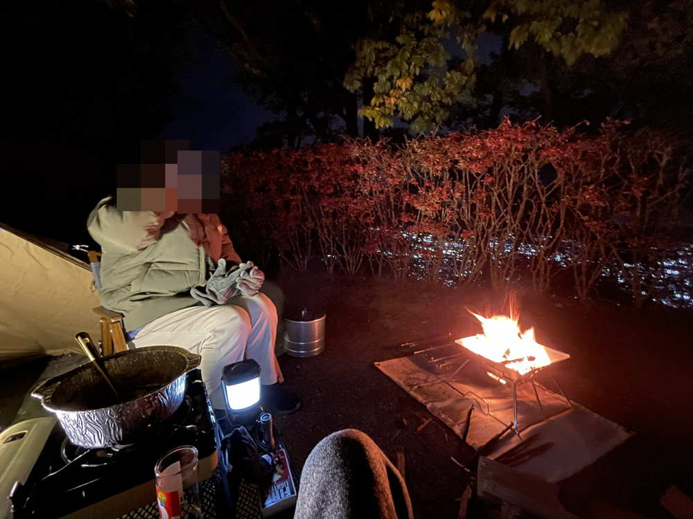夜のキャンプサイトで焚き火を楽しみながら過ごしている様子