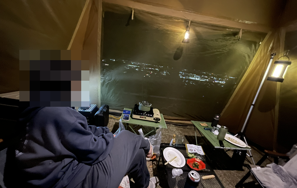 テントの中から窓越しに街の夜景を眺めながら過ごす夜キャンプ